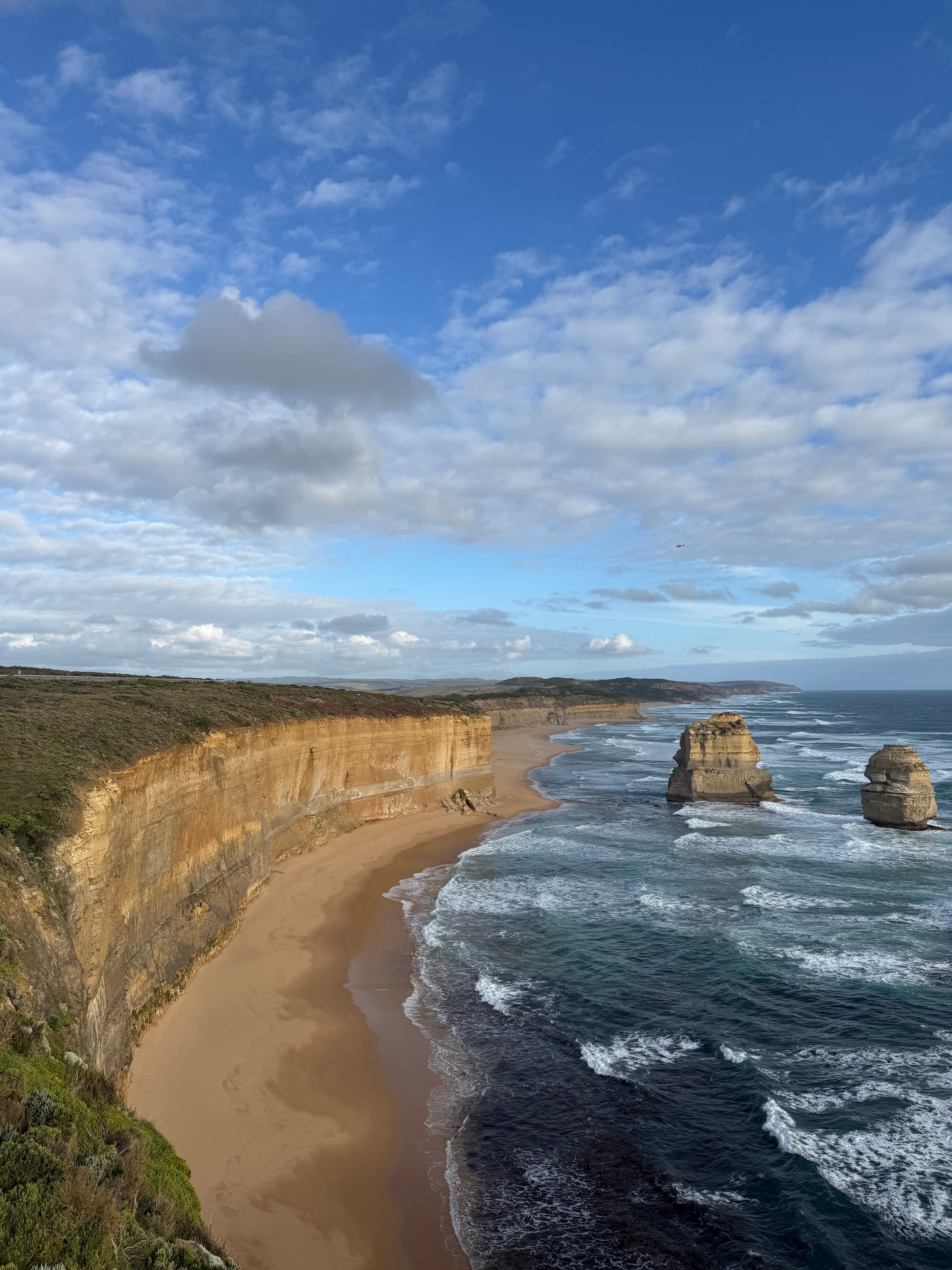 A bay seen from a clifftop, two rock stacks in the surf and a sand track running down the headland