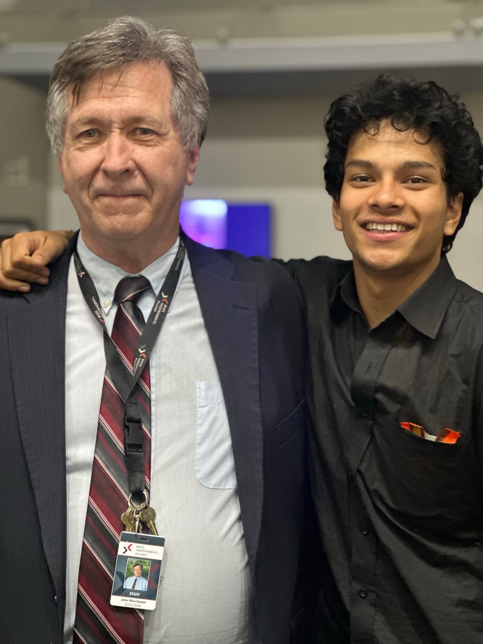 A student and a teacher standing arm in arm at a school event, the teacher wearing a staff lanyard